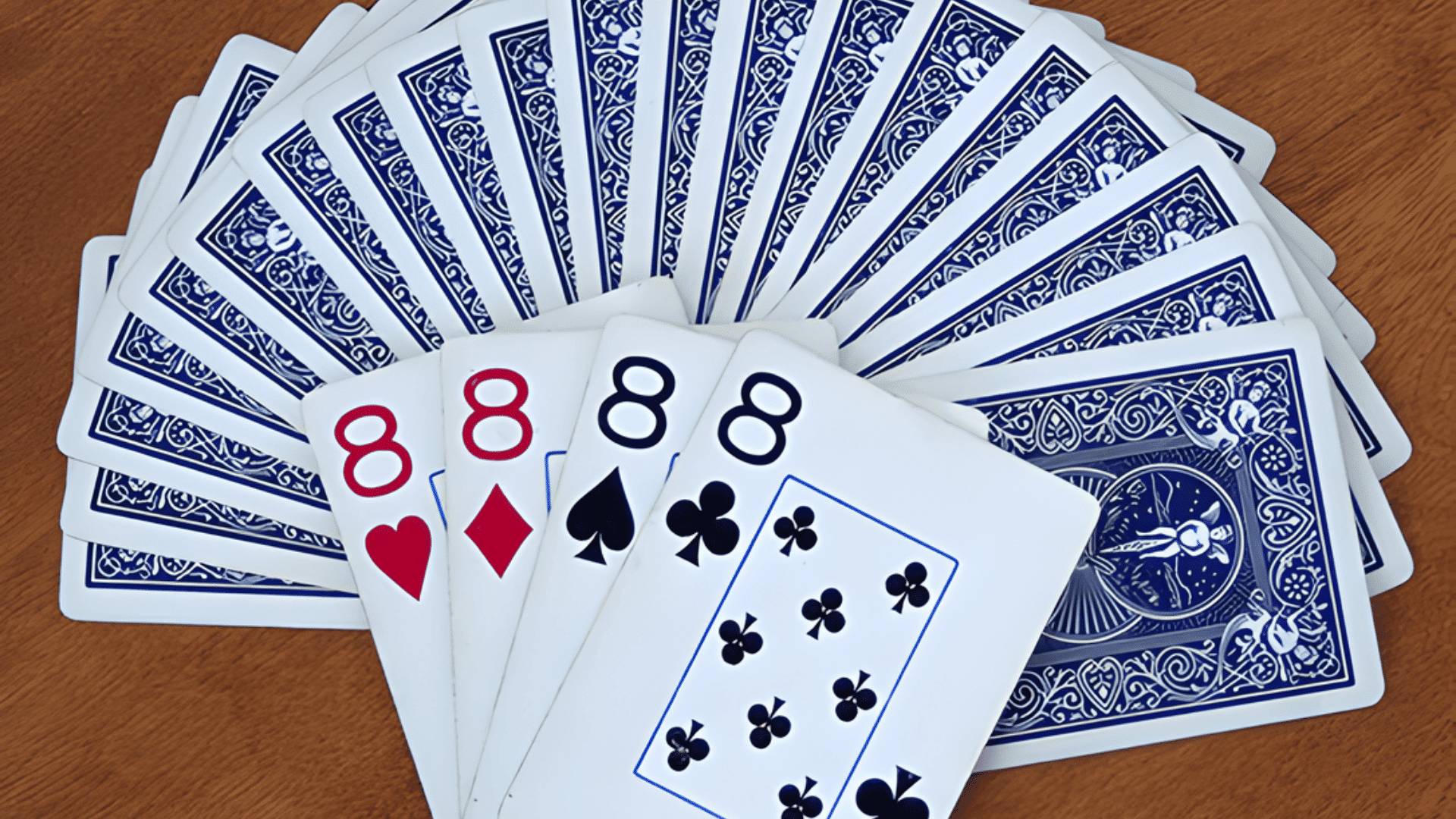 A hand of playing cards fanning out four 8s next to face-down cards with blue intricate patterns on a wood surface.