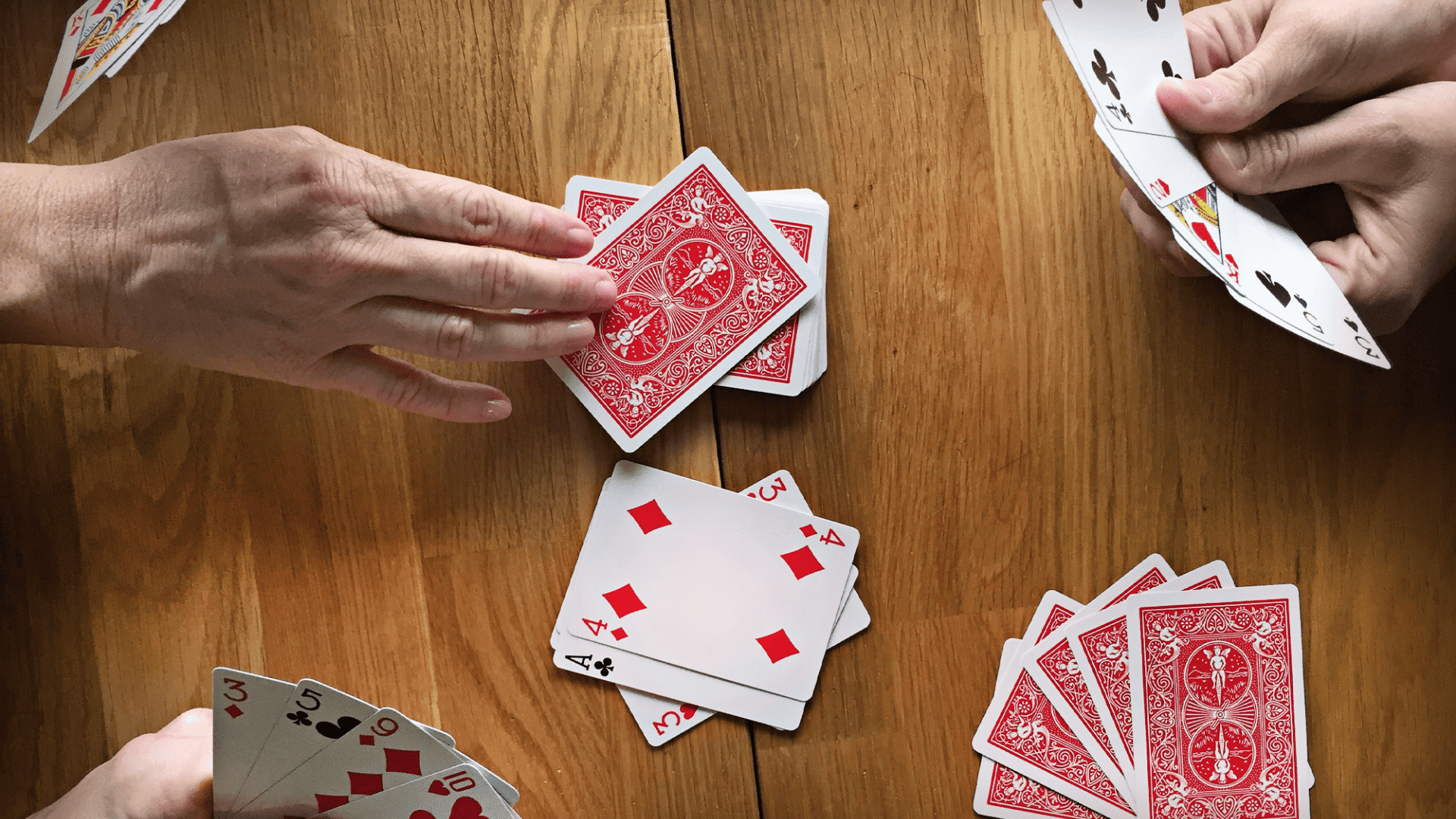 The image shows a game of gin rummy in progress on a wooden table, featuring players organizing their hands.