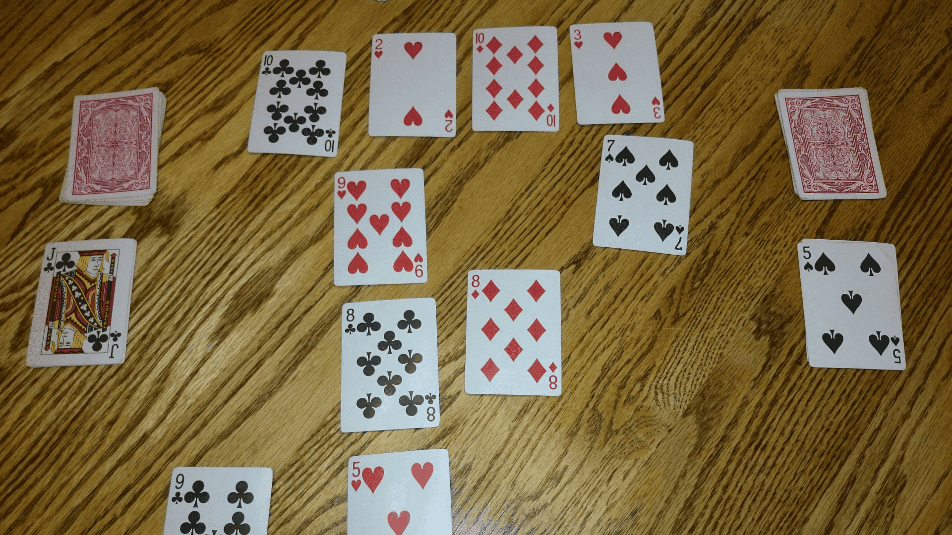 Top view of two people playing the fast-paced card game Speed with a standard deck on a wooden table.
