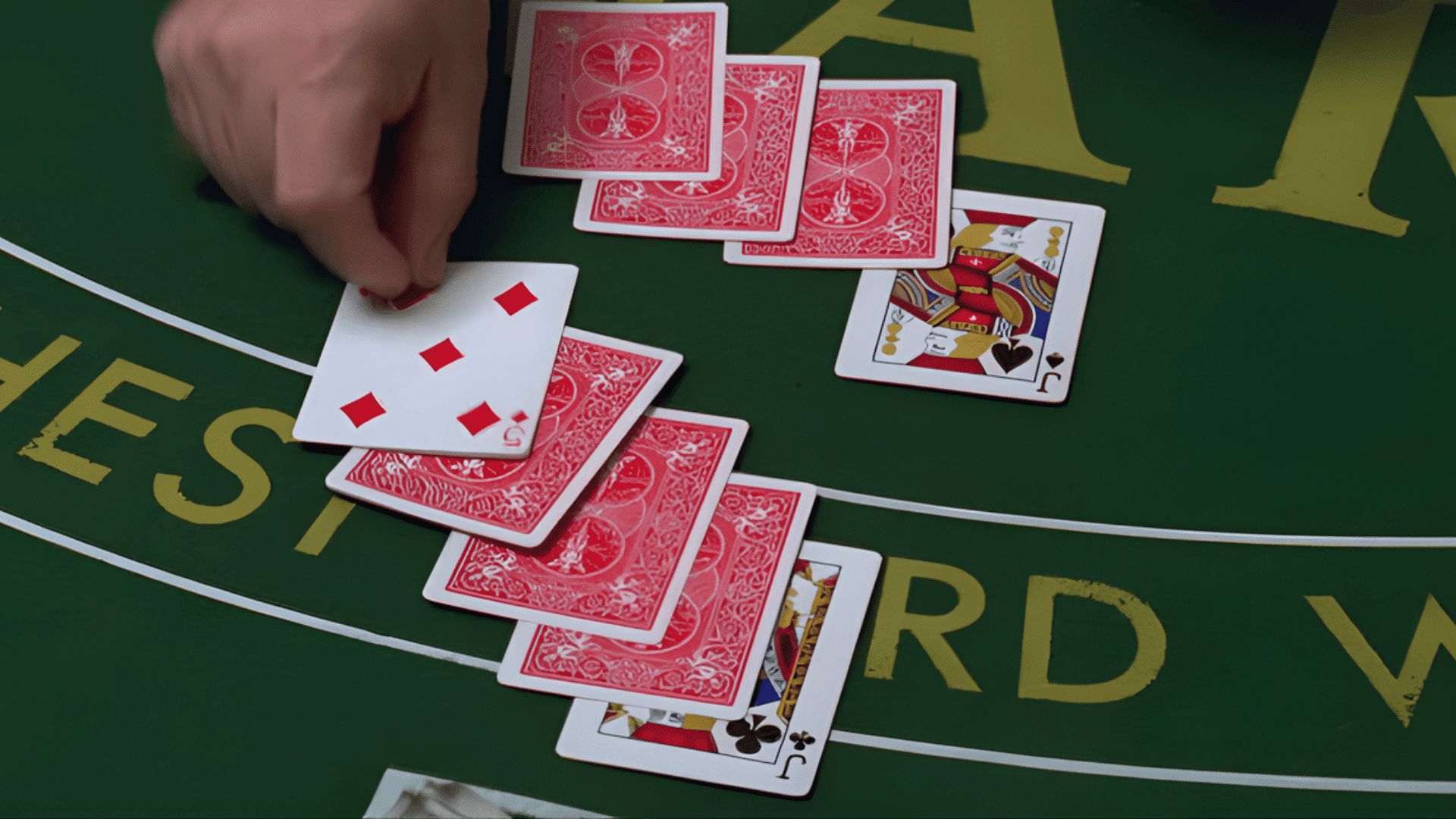 A hand spreading playing cards face up and face down on a green felt table during a trick-taking card game.